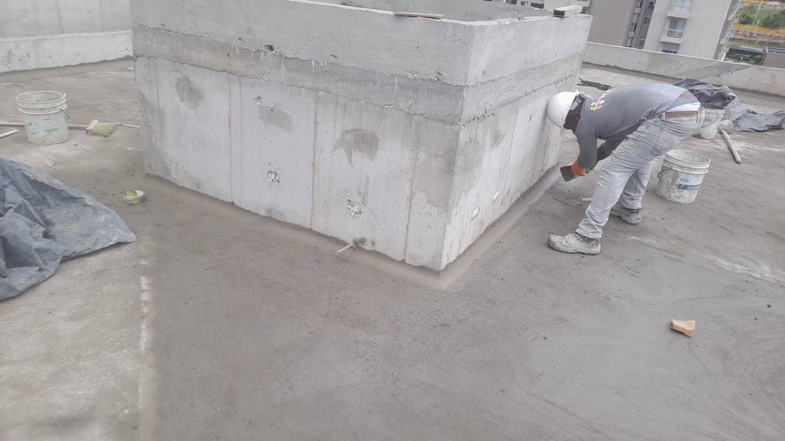 Operario formando una media caña con mortero en la base de un muro de cubierta